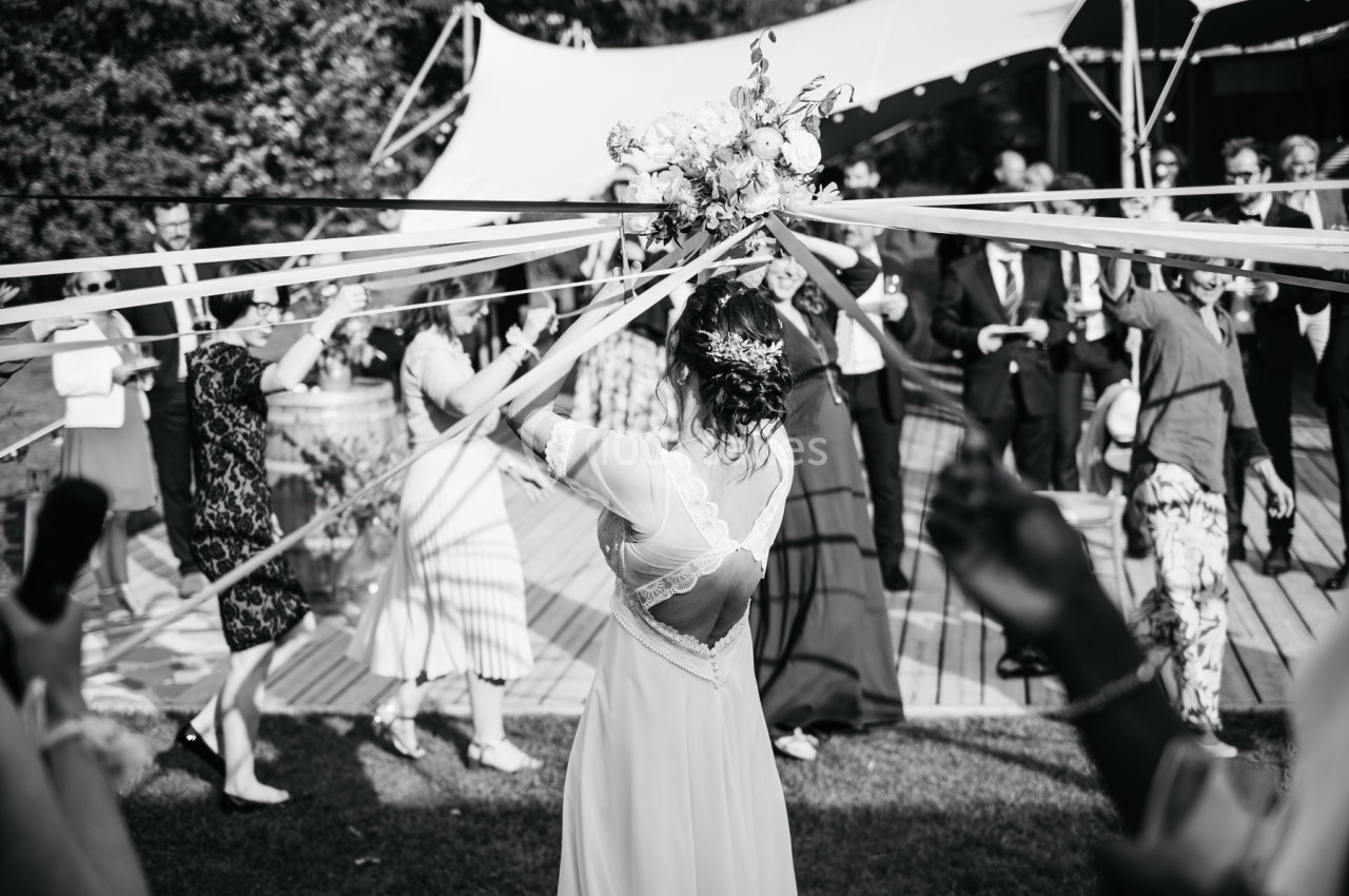 Une mariée danse en extérieur, entourée d'invités tenant des rubans, lors d'une célébration festive.