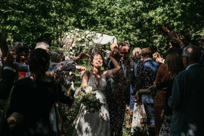 Robe de mariée en dentelle suspendue devant une fenêtre lumineuse avec vue sur un jardin verdoyant.