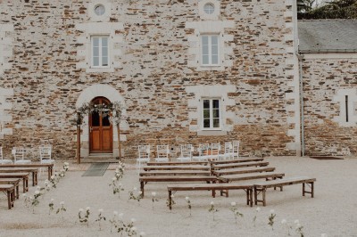 Robe de mariée en dentelle suspendue devant une fenêtre lumineuse avec vue sur un jardin verdoyant.