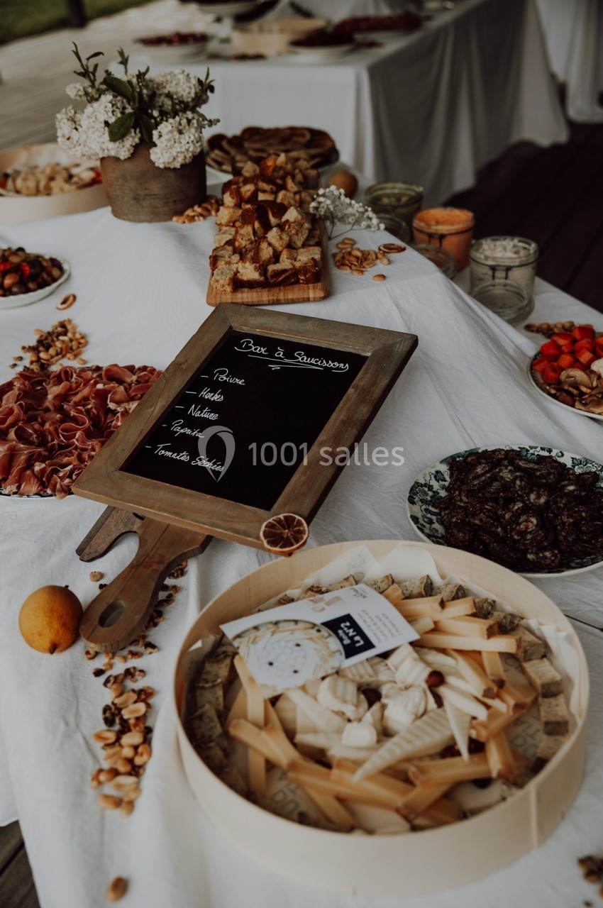 Table dressée avec des plateaux de fromages, charcuteries, fruits secs et une ardoise indiquant les options du buffet.
