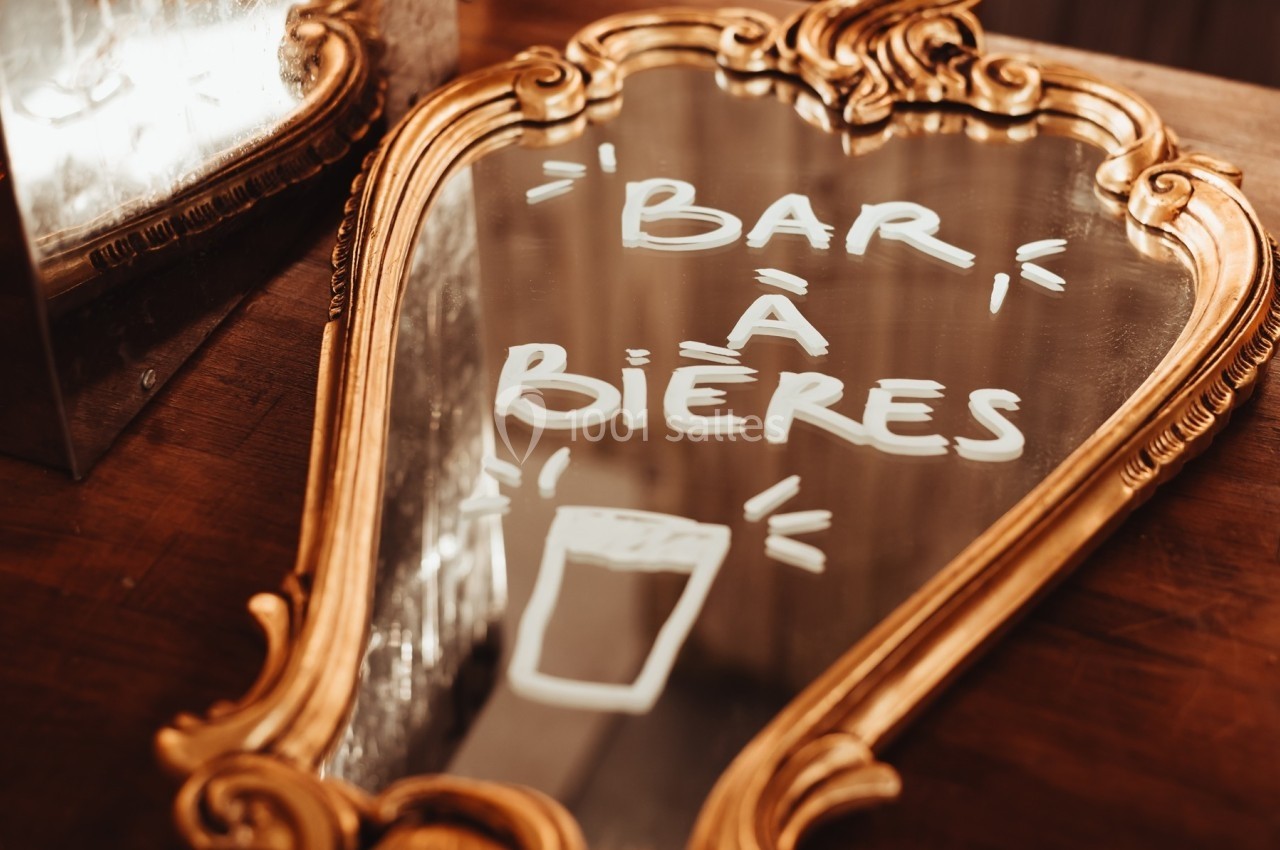 Miroir doré avec l'inscription manuscrite ’Bar à bières’ et un dessin de verre, posé sur une table en bois.