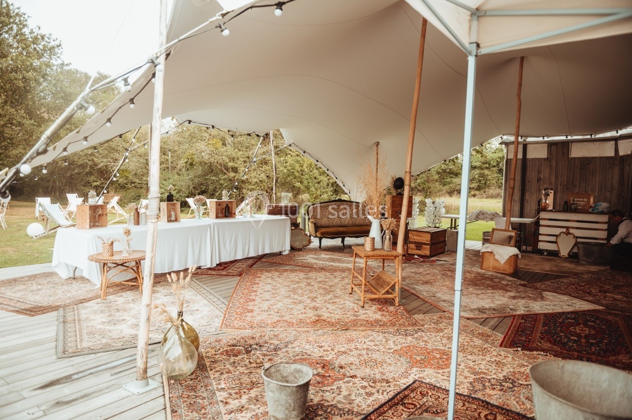 Tente blanche ouverte avec tapis colorés, mobilier en bois et décor champêtre sur une terrasse en extérieur.