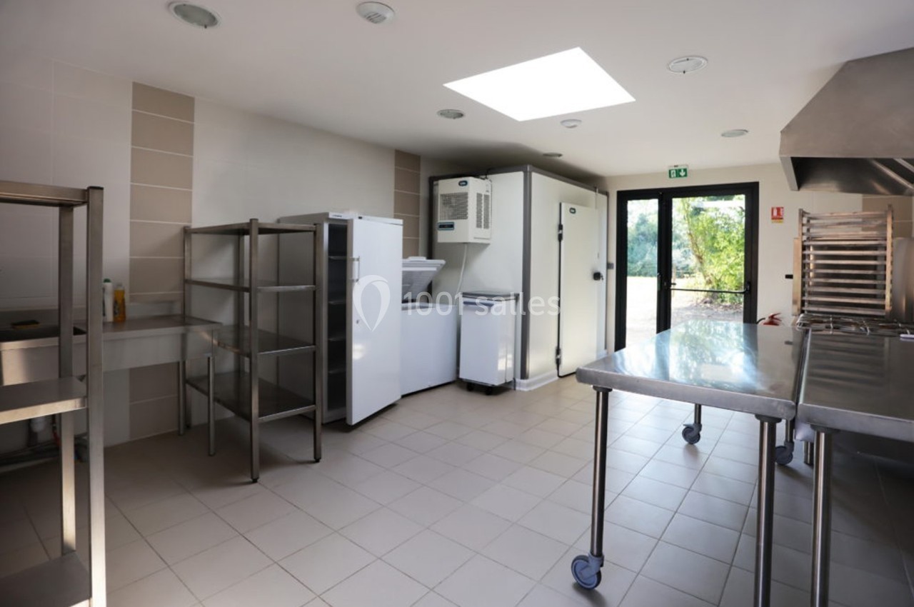 Cuisine professionnelle lumineuse avec équipements en inox, étagères, réfrigérateurs et vue sur l'extérieur.