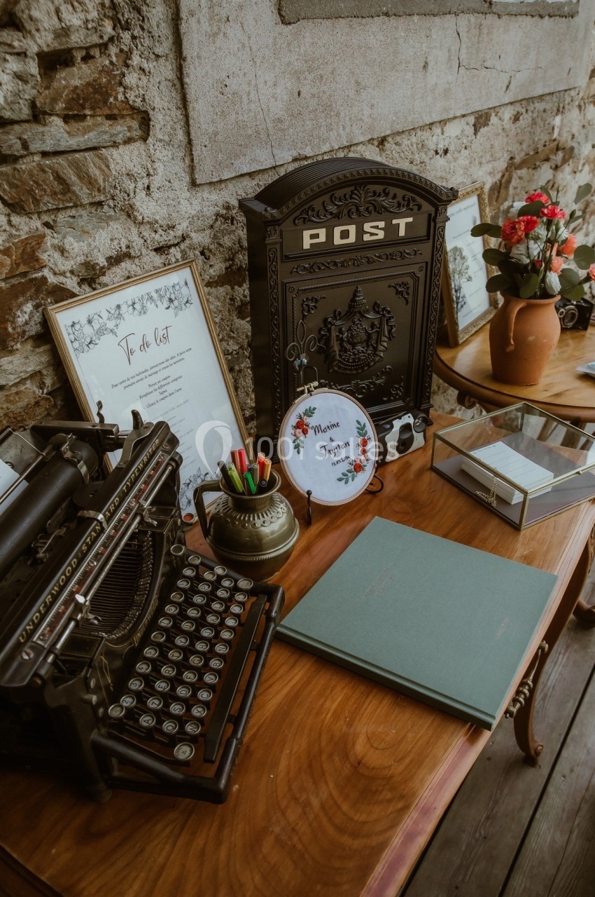 Bureau vintage avec machine à écrire, boîte aux lettres ancienne, cadres décoratifs et vase de fleurs sur une table en bois.