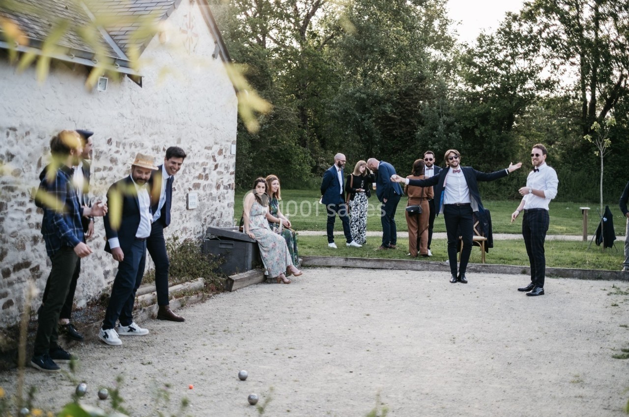 Des personnes jouent à la pétanque et discutent dans un espace extérieur près d'un bâtiment en pierre.