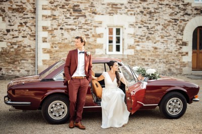 Robe de mariée en dentelle suspendue devant une fenêtre lumineuse avec vue sur un jardin verdoyant.