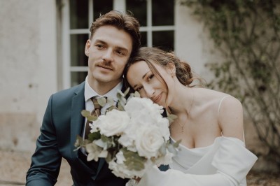 Robe de mariée en dentelle suspendue devant une fenêtre lumineuse avec vue sur un jardin verdoyant.