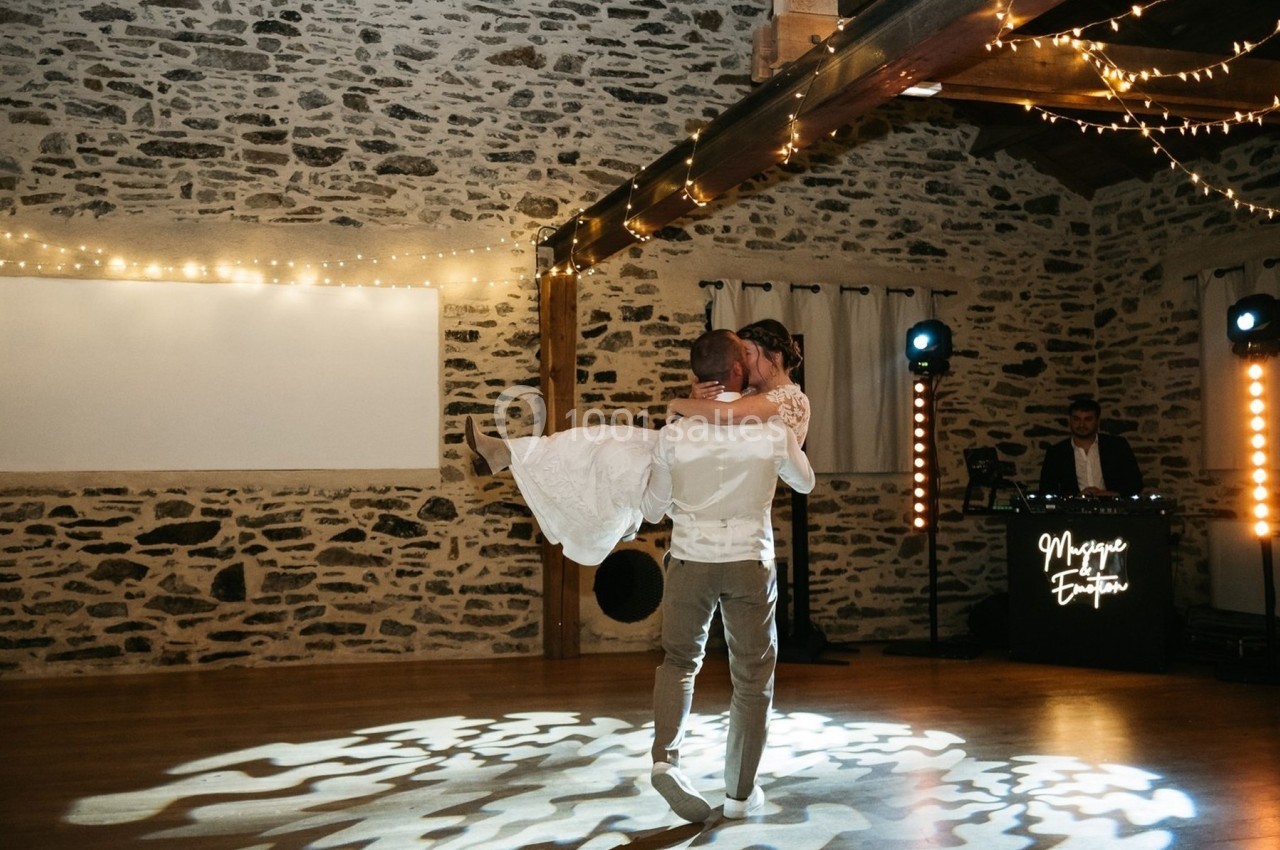Un couple danse dans une salle en pierre éclairée par des guirlandes lumineuses, avec un DJ en arrière-plan.