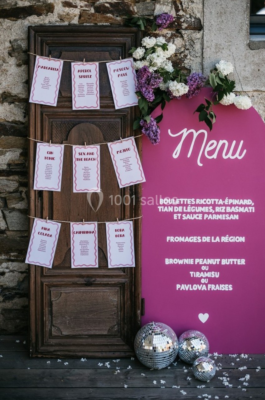 Panneau rose affichant un menu de mariage avec des cartes de cocktails suspendues sur une porte en bois, décoré de fleurs et…
