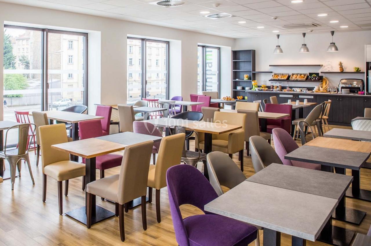 Salle de restaurant lumineuse avec tables et chaises colorées, buffet en arrière-plan et grandes fenêtres.