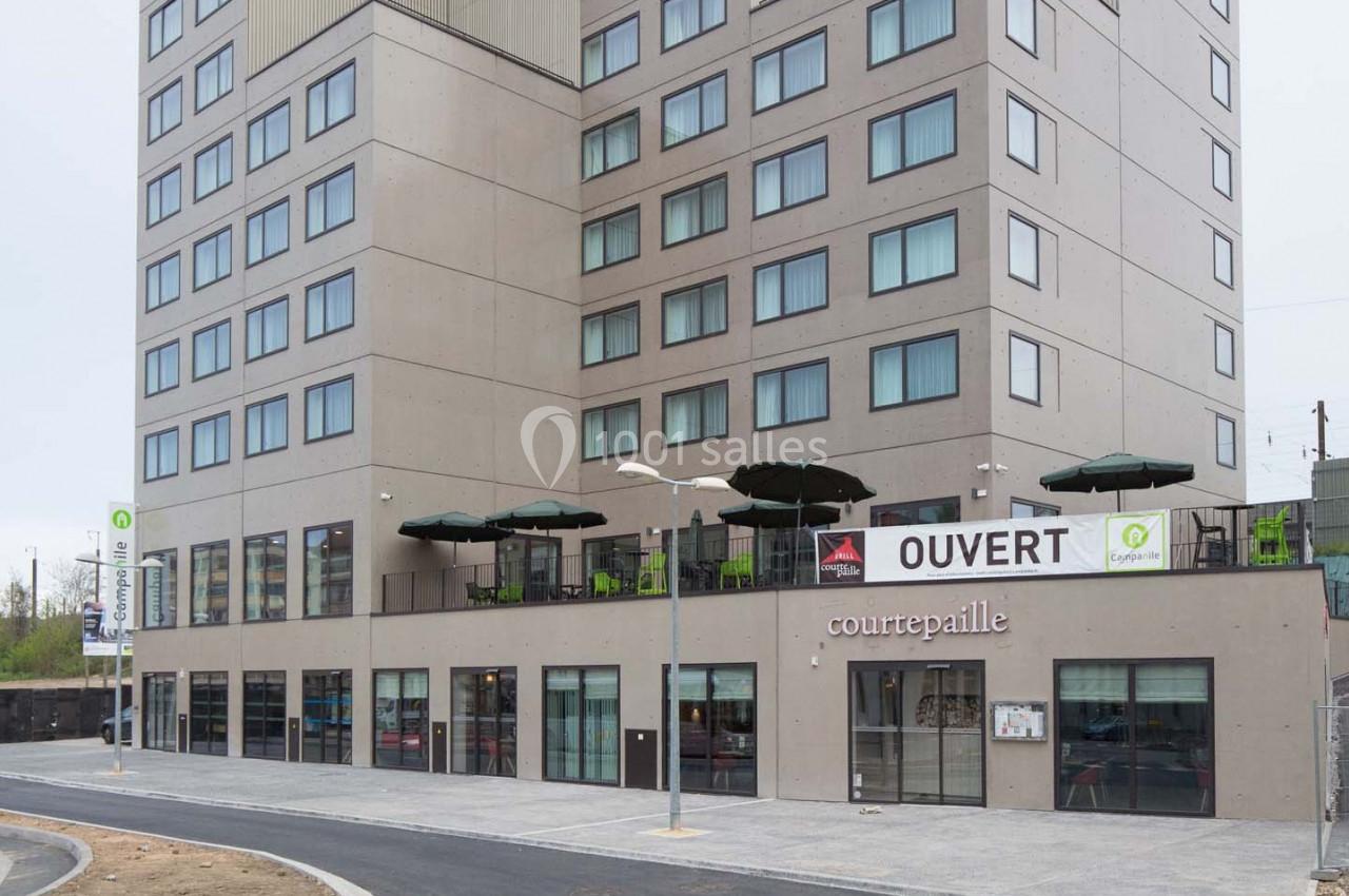 Façade d'un restaurant Courtepaille avec terrasse et enseigne ’OUVERT’, situé au rez-de-chaussée d'un immeuble moderne.