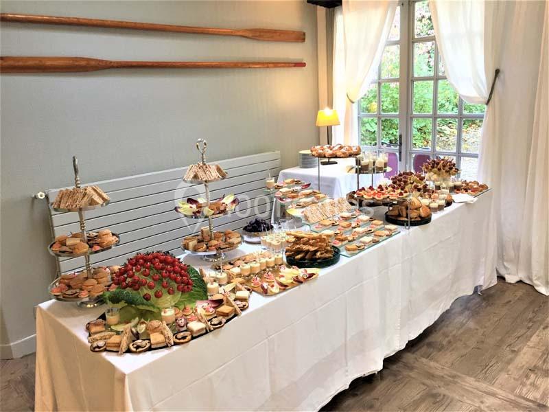 Table garnie d'un buffet varié comprenant desserts, fruits et amuse-bouches dans une salle lumineuse.