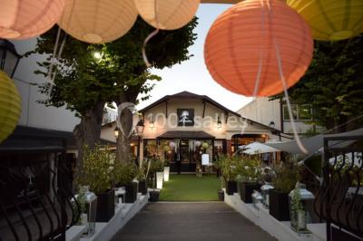 Terrasse extérieure avec tables dressées sous des parasols, entourée de verdure et visible à travers une fenêtre.