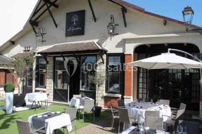 Terrasse extérieure avec tables dressées sous des parasols, entourée de verdure et visible à travers une fenêtre.
