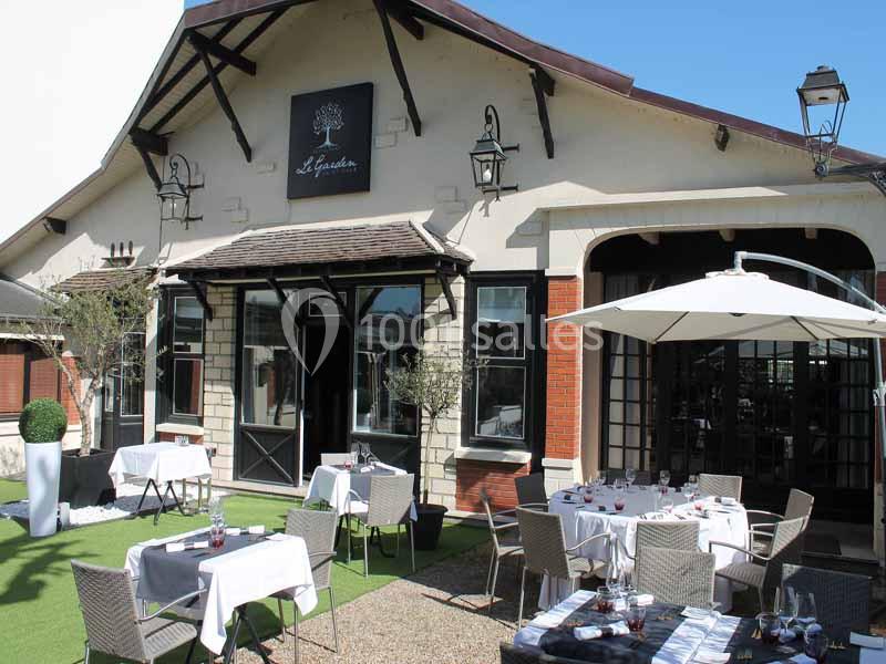 Terrasse d'un restaurant avec tables dressées, parasols blancs et façade en briques et bois.