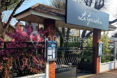 Terrasse extérieure avec tables dressées sous des parasols, entourée de verdure et visible à travers une fenêtre.