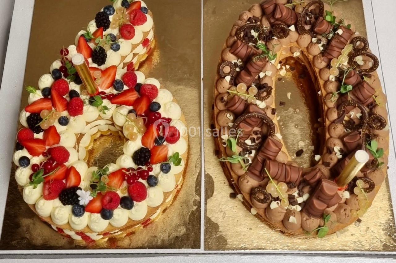 Deux gâteaux en forme de chiffres décorés de fruits rouges, fleurs comestibles et chocolats sur un plateau doré.