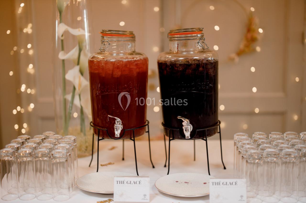 Deux distributeurs de thé glacé, rouge et noir, entourés de verres vides sur une table décorée.