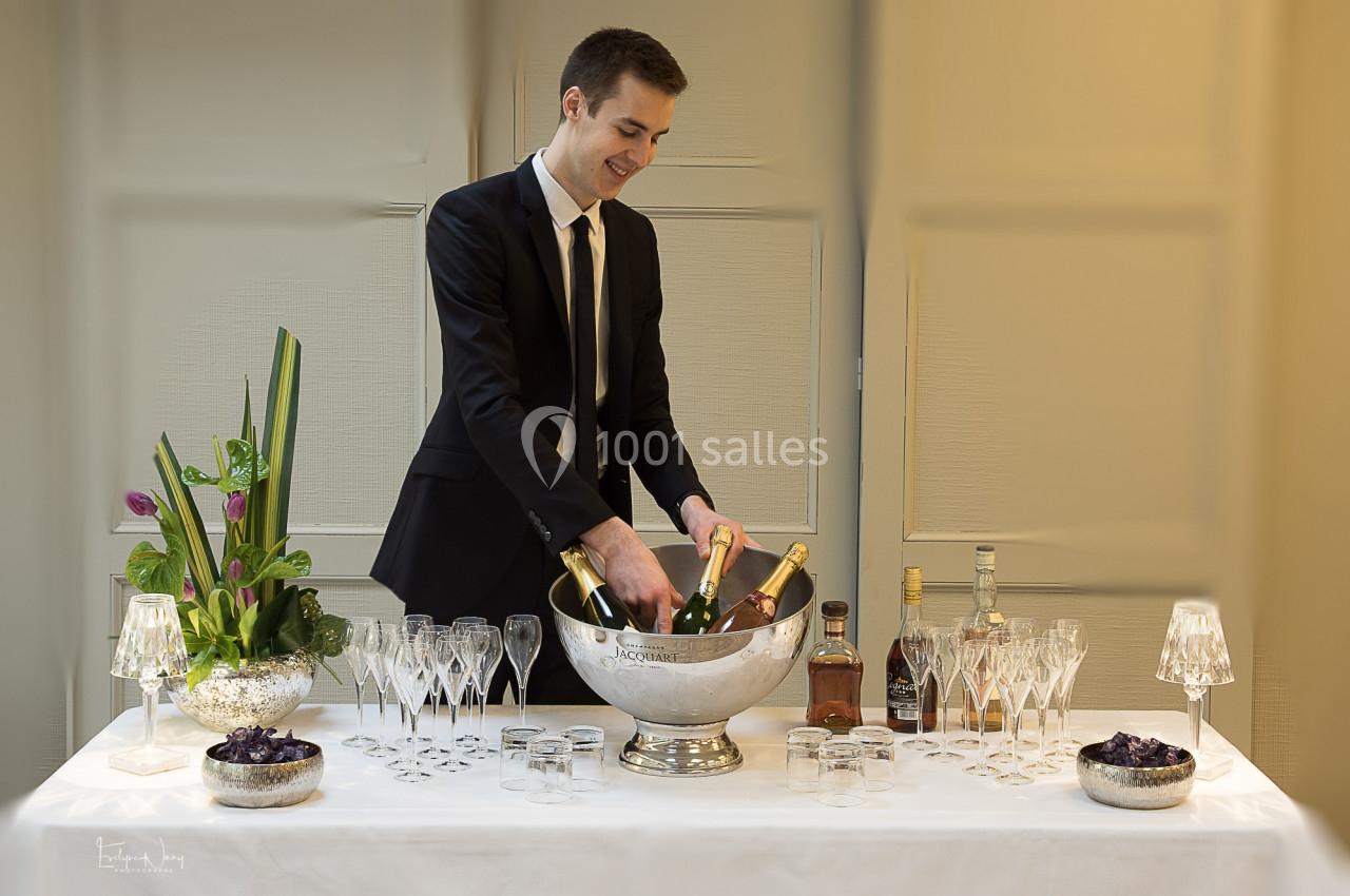 Un serveur en costume prépare des bouteilles de champagne dans un seau à glace sur une table dressée.