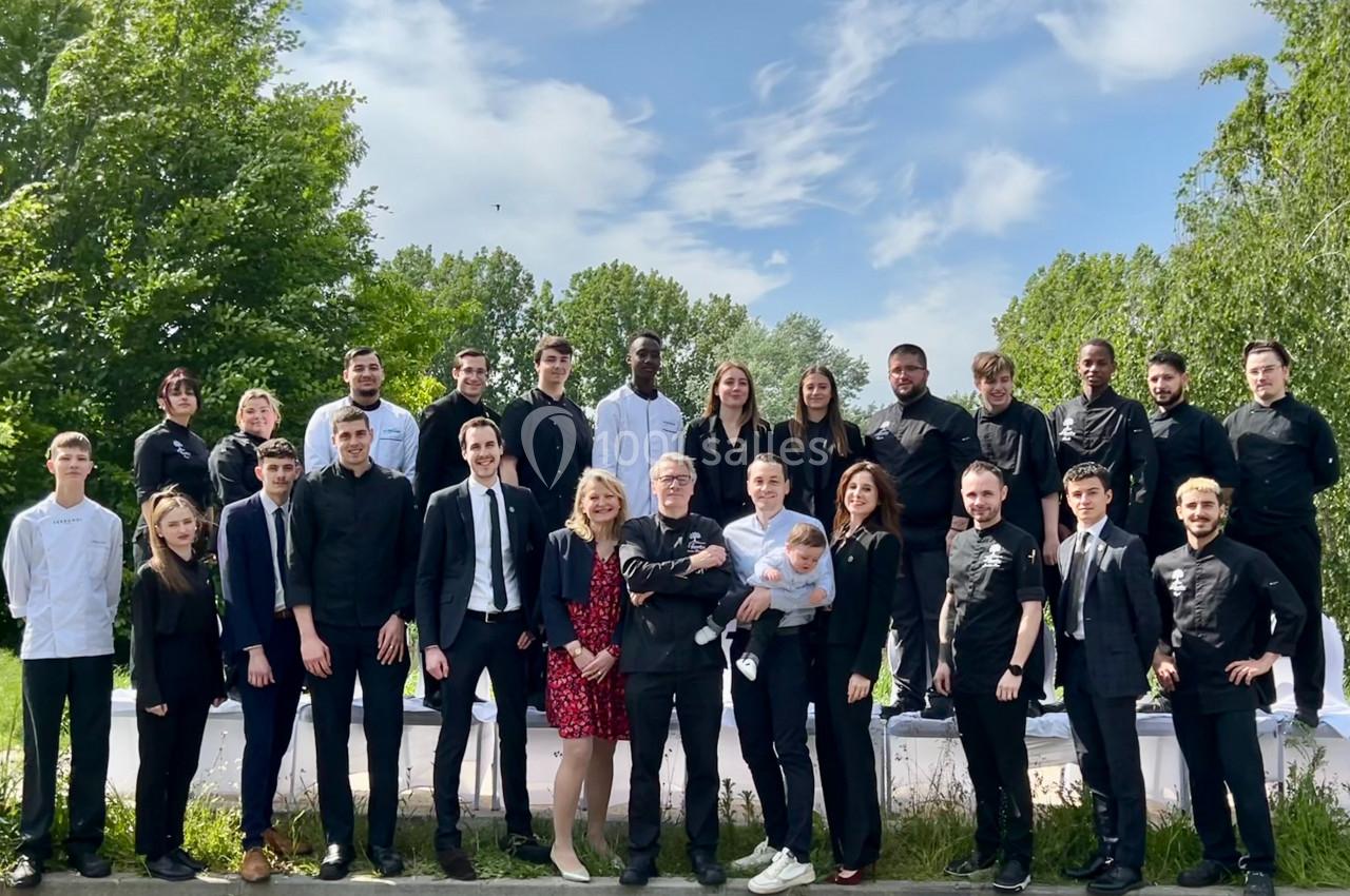 Un groupe de personnes en tenue professionnelle posant à l'extérieur devant des arbres et un ciel dégagé.