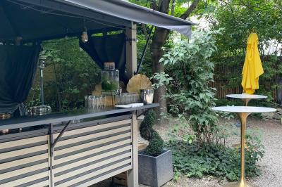Terrasse extérieure avec tables dressées sous des parasols, entourée de verdure et visible à travers une fenêtre.