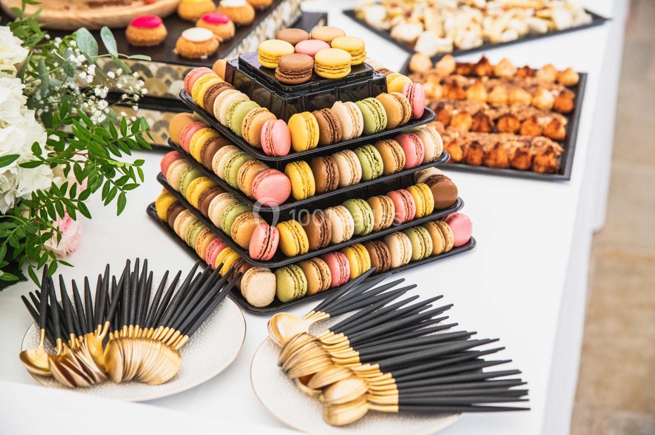 Pyramide de macarons colorés sur une table de buffet, entourée de couverts et de pâtisseries variées.