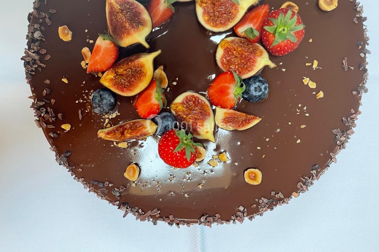 Gâteau au glaçage chocolat brillant, décoré de figues fraîches, fraises, myrtilles et noisettes concassées.