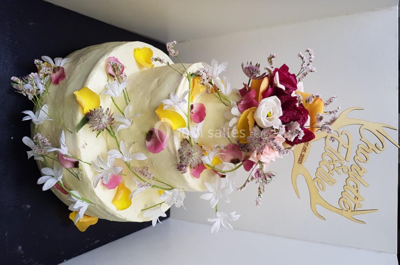 Gâteau à étages décoré de fleurs fraîches colorées et d'un panneau doré avec une inscription festive.