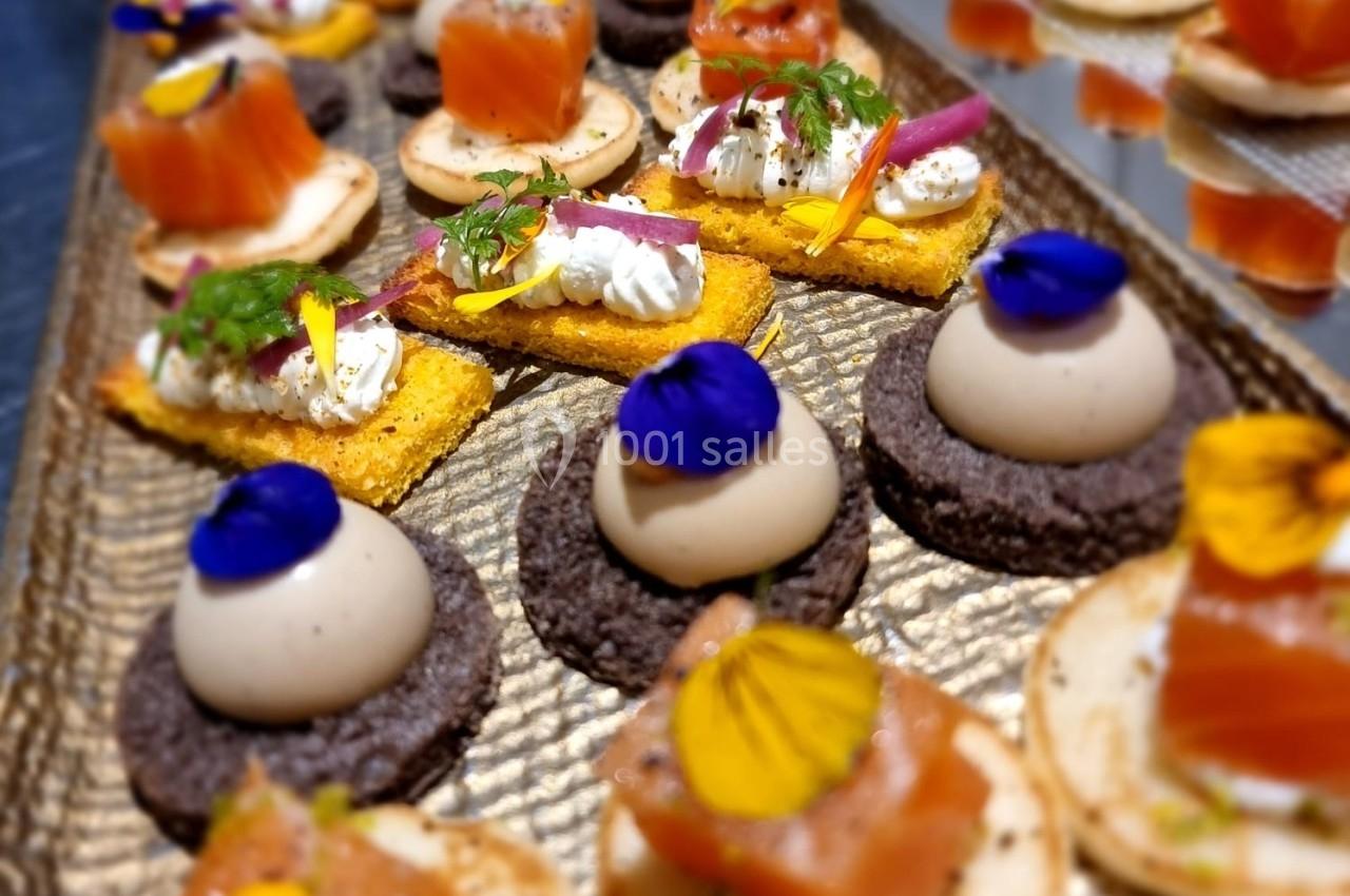 Assortiment de canapés raffinés avec saumon, mousse et décorations florales sur un plateau doré.