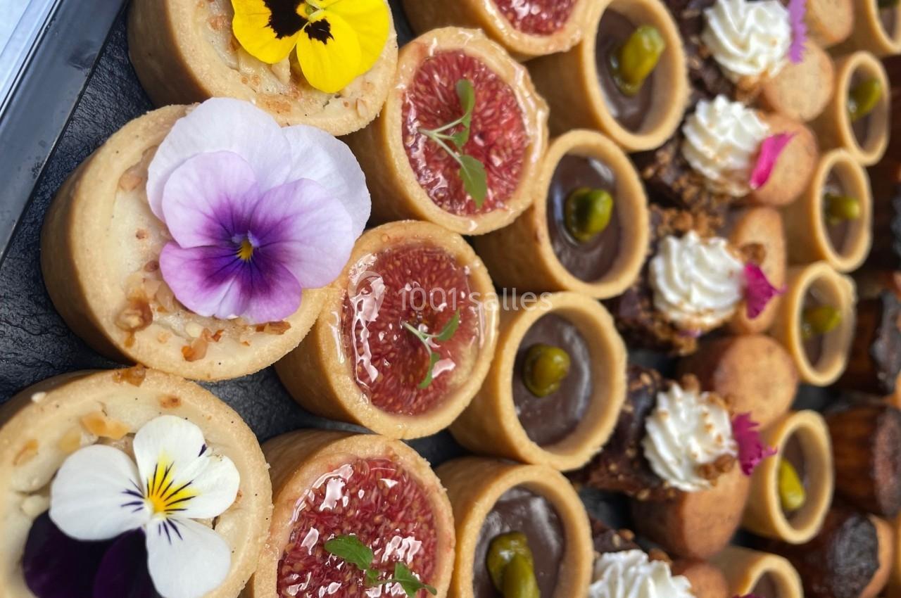 Assortiment de tartelettes garnies de fruits, crème et fleurs comestibles, disposées sur un plateau.
