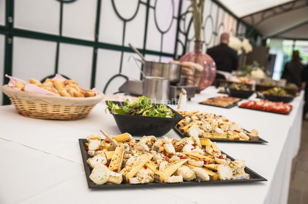 Plateaux de fromages variés et salade verte disposés sur une table de buffet avec paniers de pain en arrière-plan.