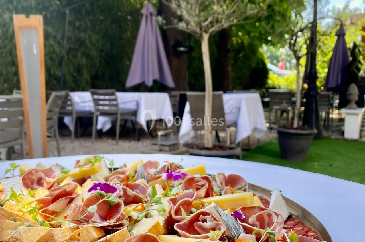 Plateau de charcuterie et fromages décoré de fleurs comestibles, présenté sur une table en terrasse ombragée.