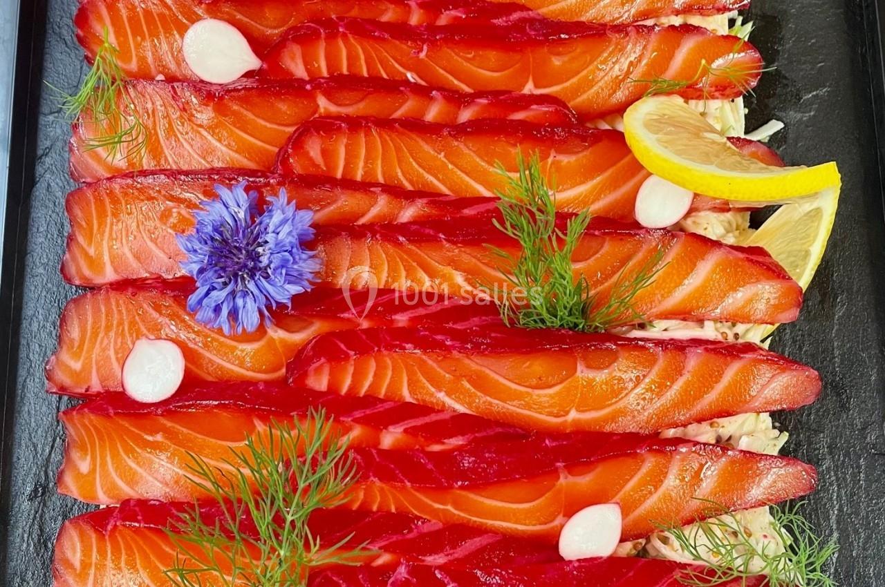 Tranches de saumon gravlax rouge vif garnies d'aneth, fleurs bleues, rondelles de citron et touches de crème blanche.