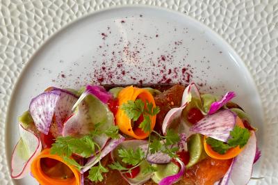 Terrasse extérieure avec tables dressées sous des parasols, entourée de verdure et visible à travers une fenêtre.