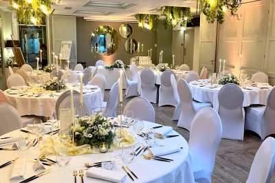 Terrasse extérieure avec tables dressées sous des parasols, entourée de verdure et visible à travers une fenêtre.