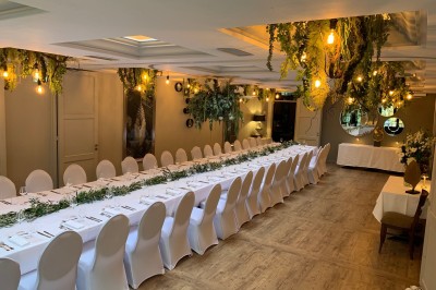Terrasse extérieure avec tables dressées sous des parasols, entourée de verdure et visible à travers une fenêtre.