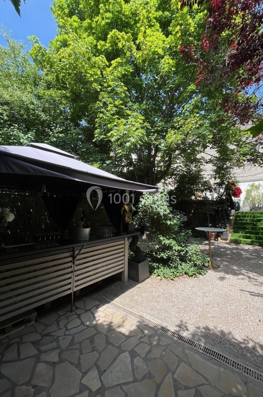 Terrasse ombragée avec un bar en bois, entourée de végétation dense et éclairée par une lumière naturelle.