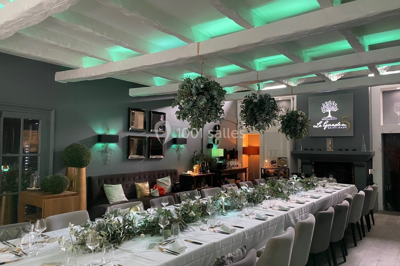 Salle de restaurant élégante avec une longue table dressée, décorée de plantes suspendues et éclairée par des lumières…