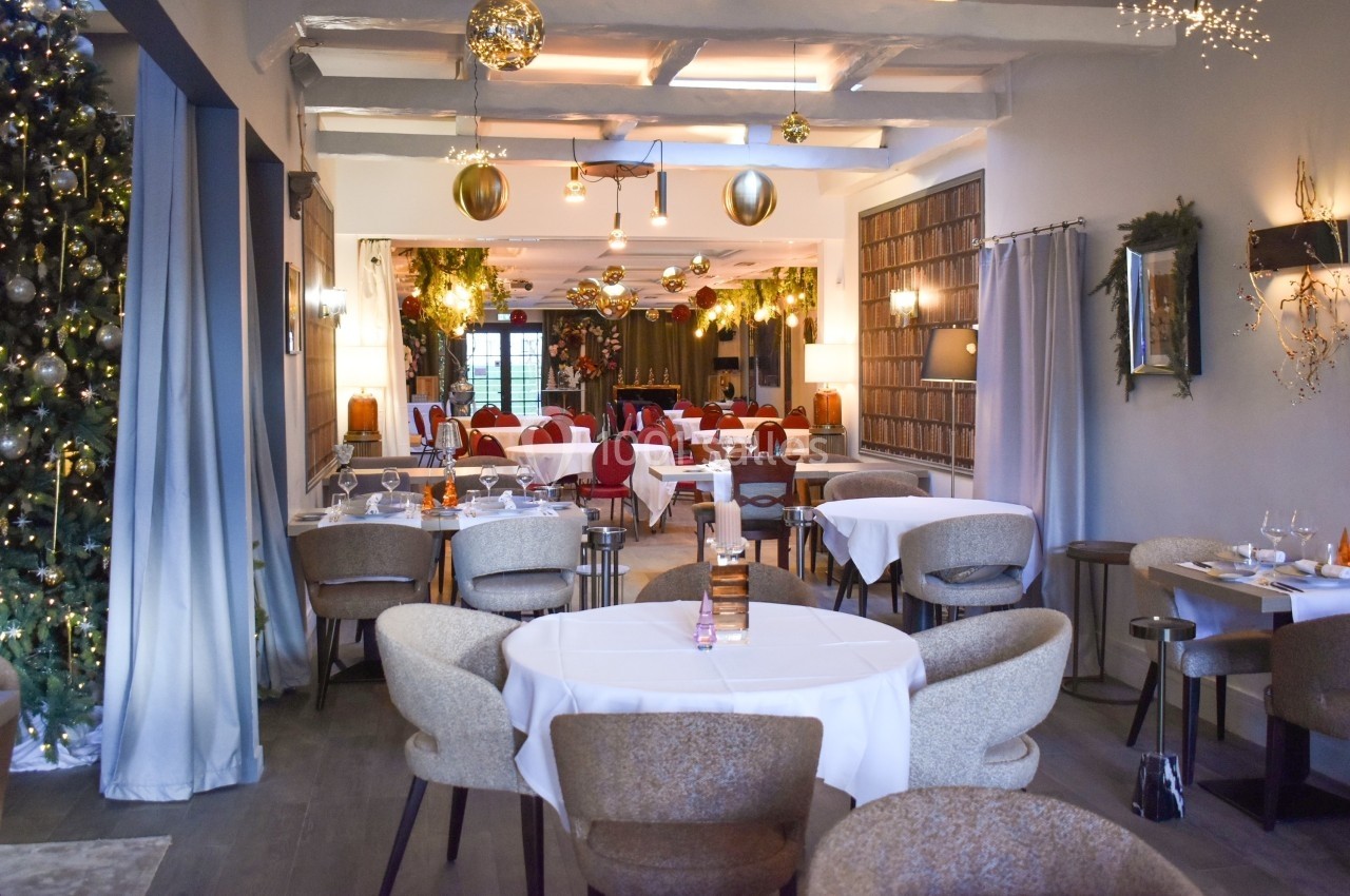 Salle de restaurant décorée pour les fêtes avec tables dressées, guirlandes lumineuses et sapin de Noël.