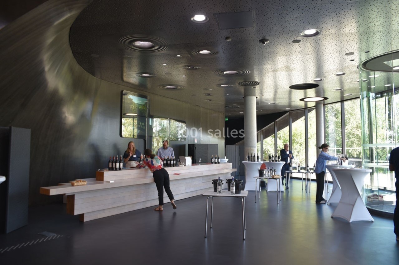 Un espace moderne avec un comptoir de dégustation de vins, des tables hautes et de grandes baies vitrées donnant sur l…