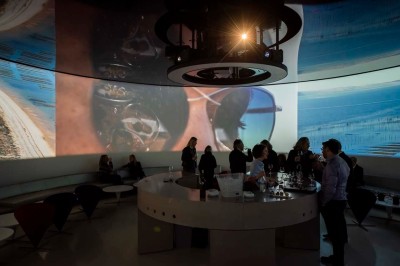 Flacons et éléments décoratifs sous cloches en verre sur une table éclairée dans un espace moderne et tamisé.