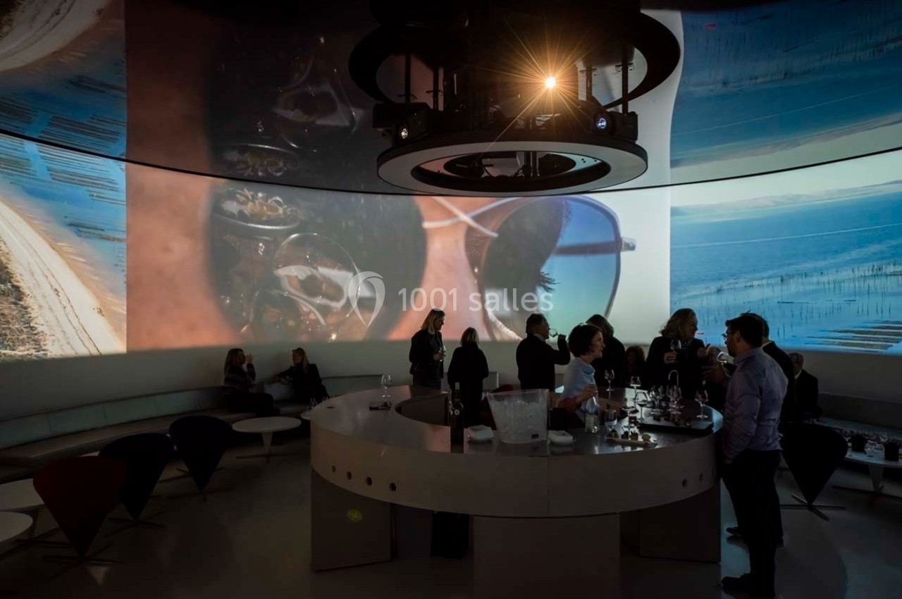 Des personnes discutent autour d'un comptoir dans une salle sombre avec des projections murales de paysages.