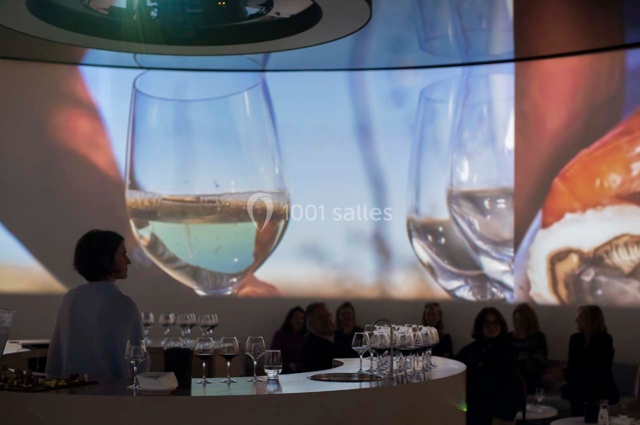 Des personnes assises dans une salle sombre avec des projections de verres de vin et d'huîtres en arrière-plan.
