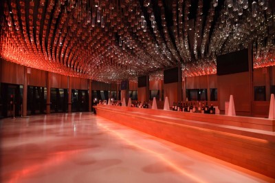 Flacons et éléments décoratifs sous cloches en verre sur une table éclairée dans un espace moderne et tamisé.