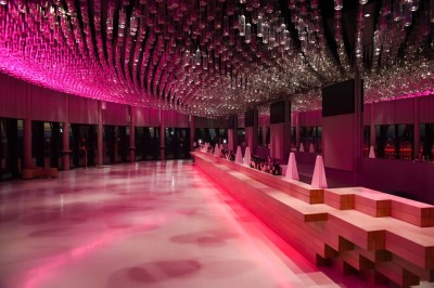 Flacons et éléments décoratifs sous cloches en verre sur une table éclairée dans un espace moderne et tamisé.