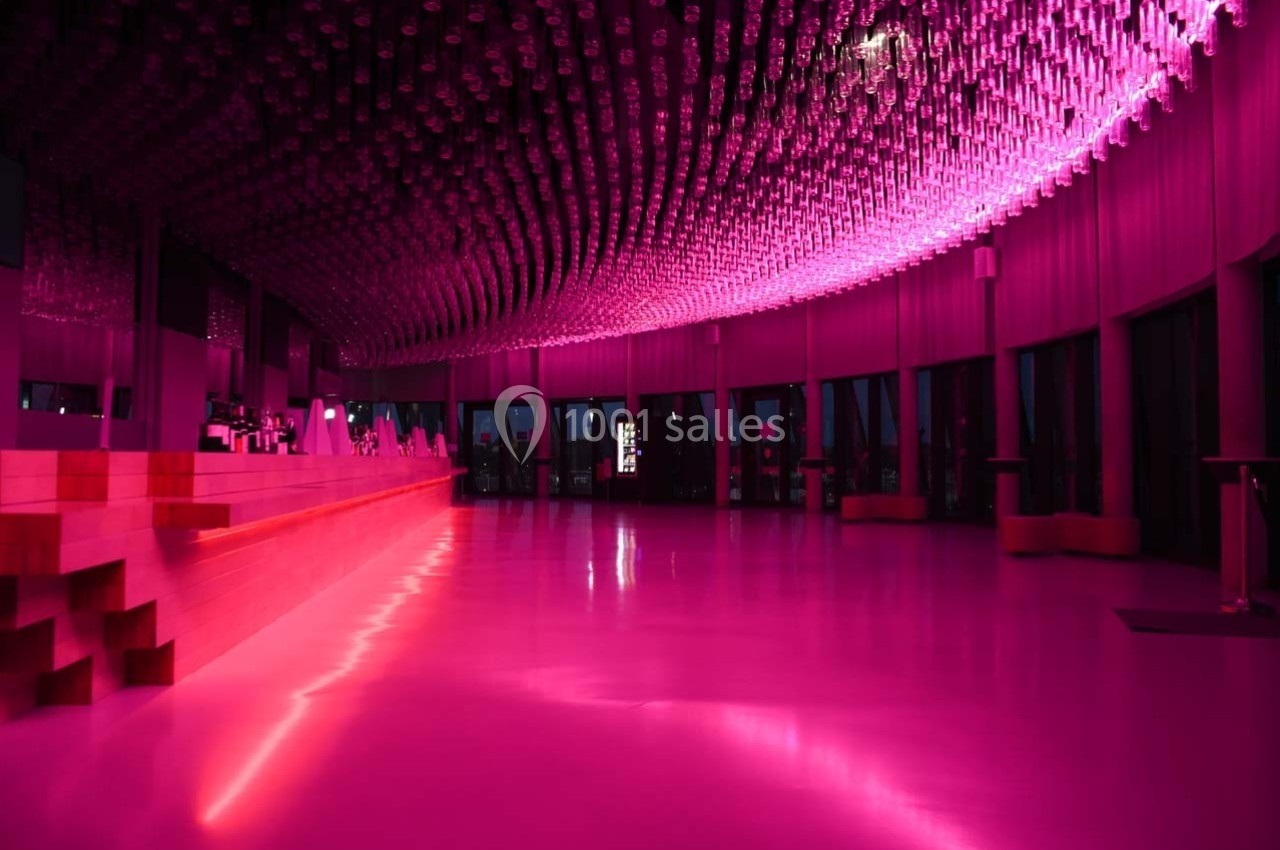 Salle moderne avec un plafond lumineux composé de nombreuses suspensions roses, éclairant un espace ouvert et épuré.