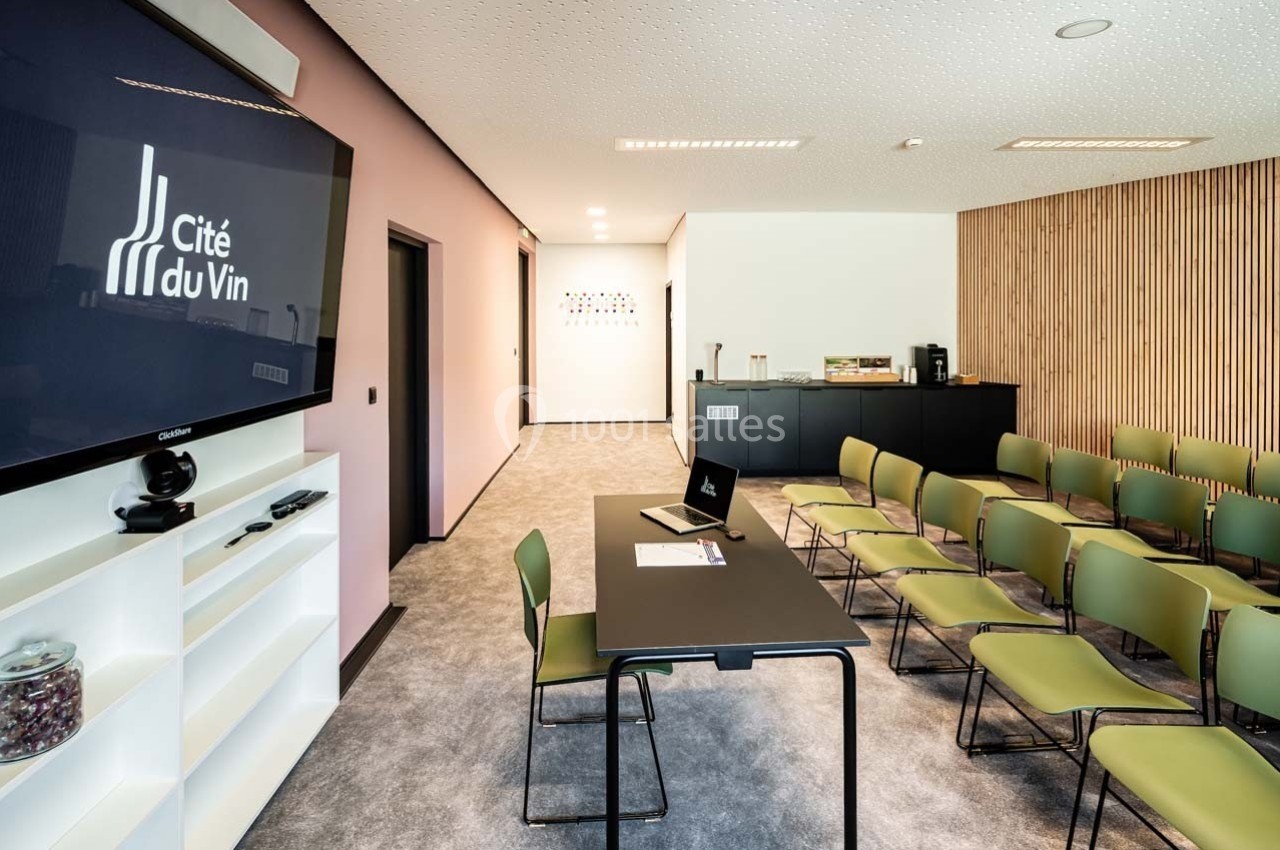 Salle de réunion moderne avec chaises alignées, table équipée et écran affichant ’Cité du Vin’ sur le mur.