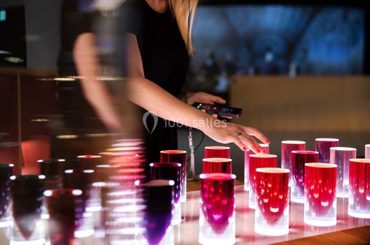 Une personne ajuste des bougies colorées illuminées sur une table dans un environnement moderne et tamisé.