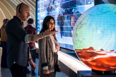 Flacons et éléments décoratifs sous cloches en verre sur une table éclairée dans un espace moderne et tamisé.
