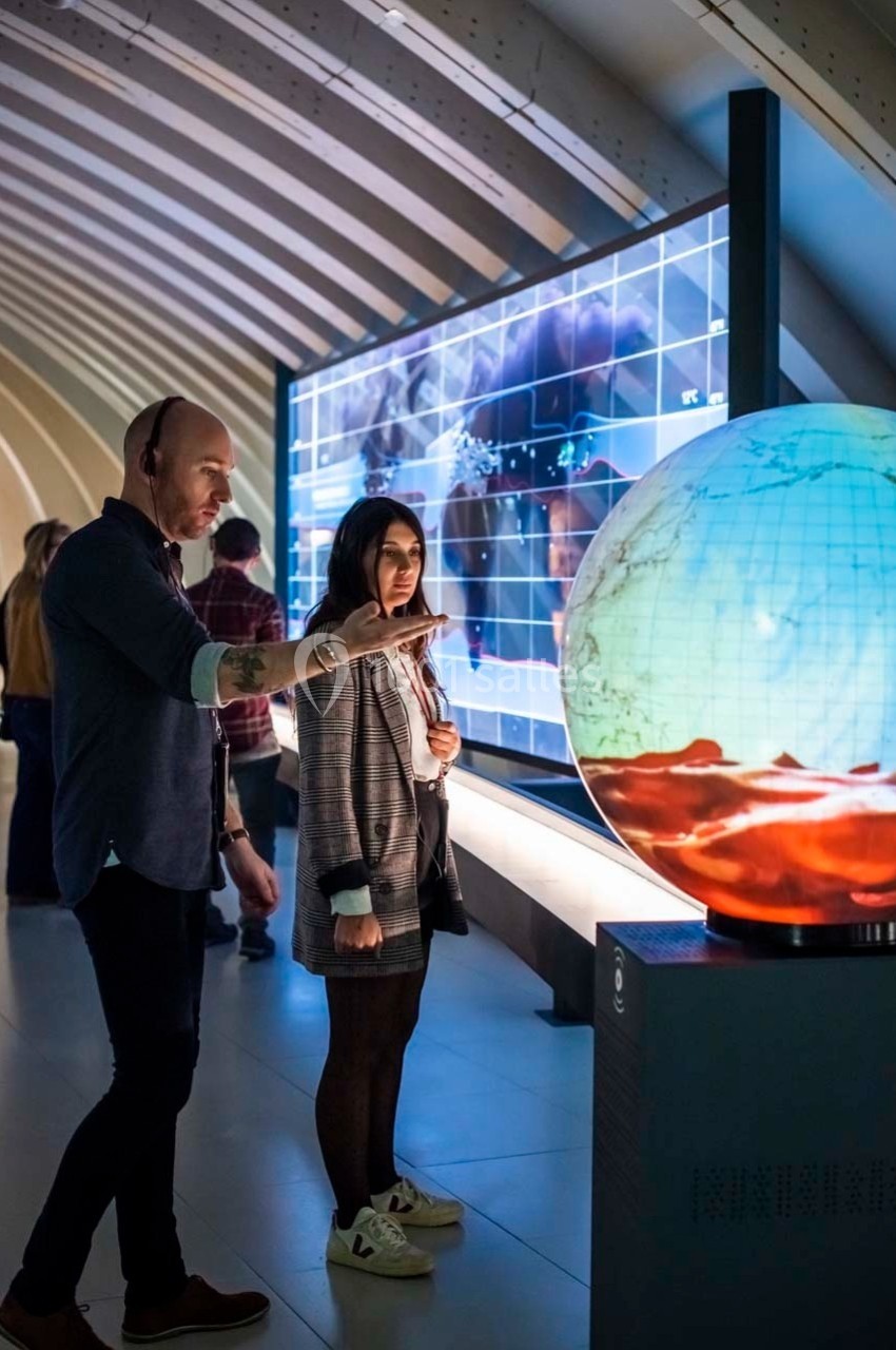 Un homme et une femme observent un globe interactif illuminé dans un espace d'exposition moderne.